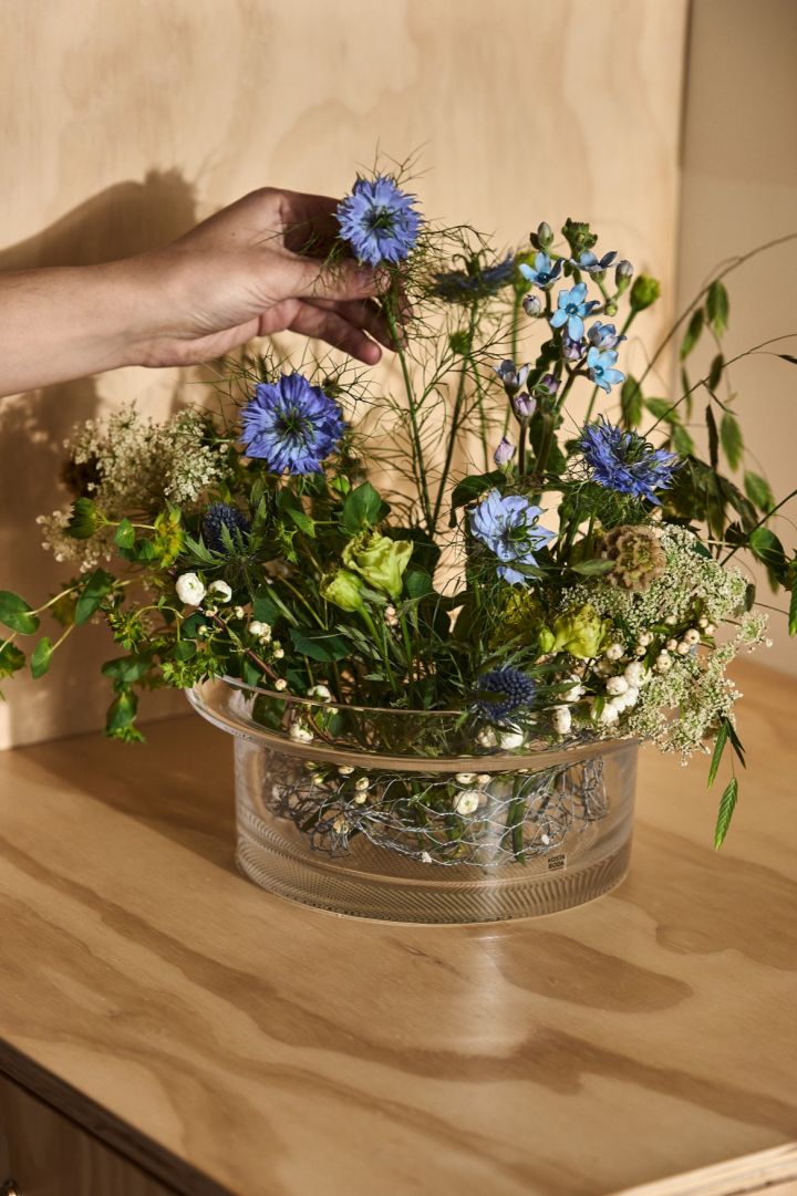 A hand places a blue cornflower into a vase from the Limelight collection from Kosta Boda.