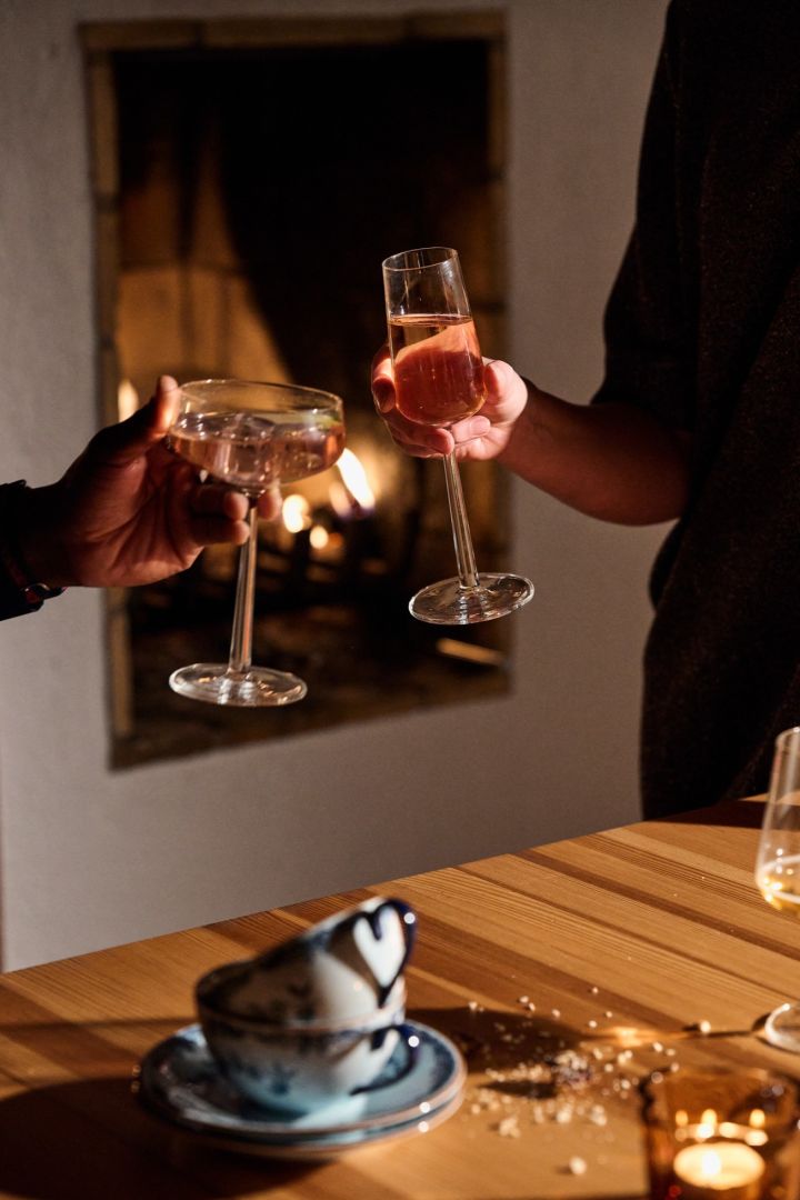 Hands cheers with two Iittala Essence glasses in front of a fire during a Nordic Christmas celebration. 