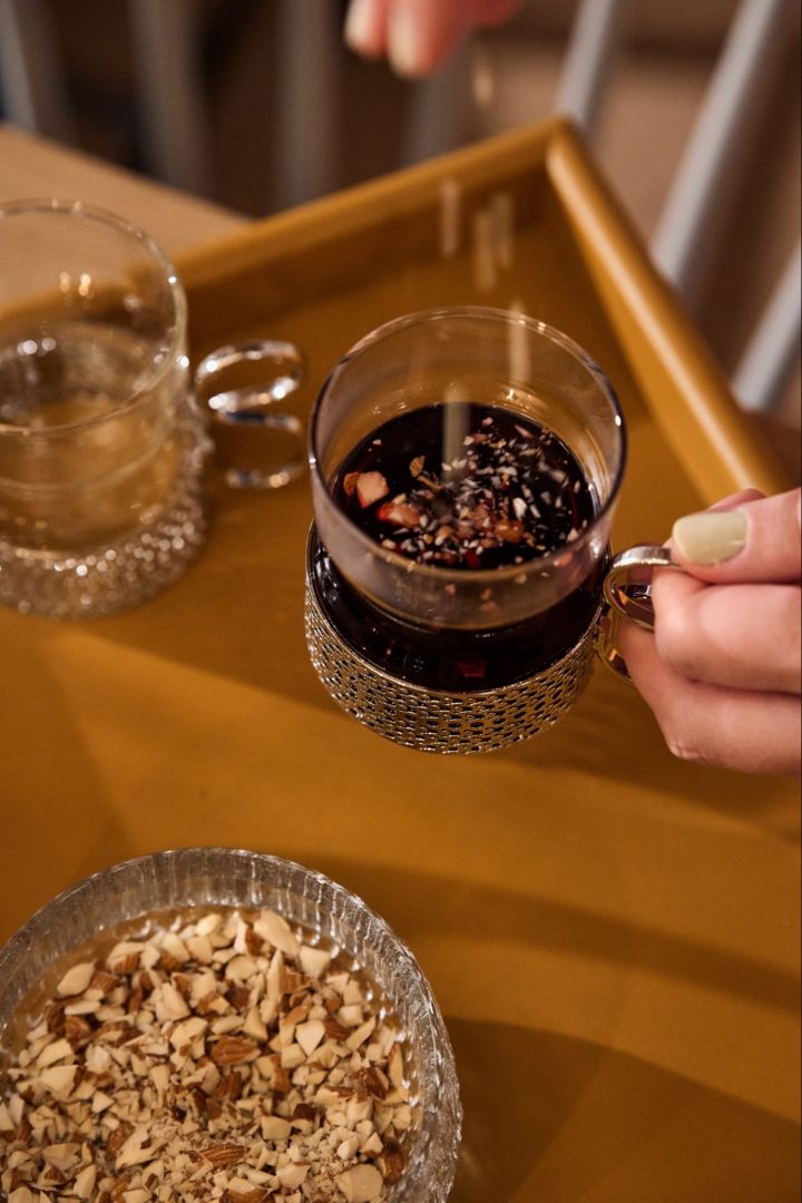 A hand sprinkles almonds into a traditional glass of glögg on a Nordic Christmas table. 