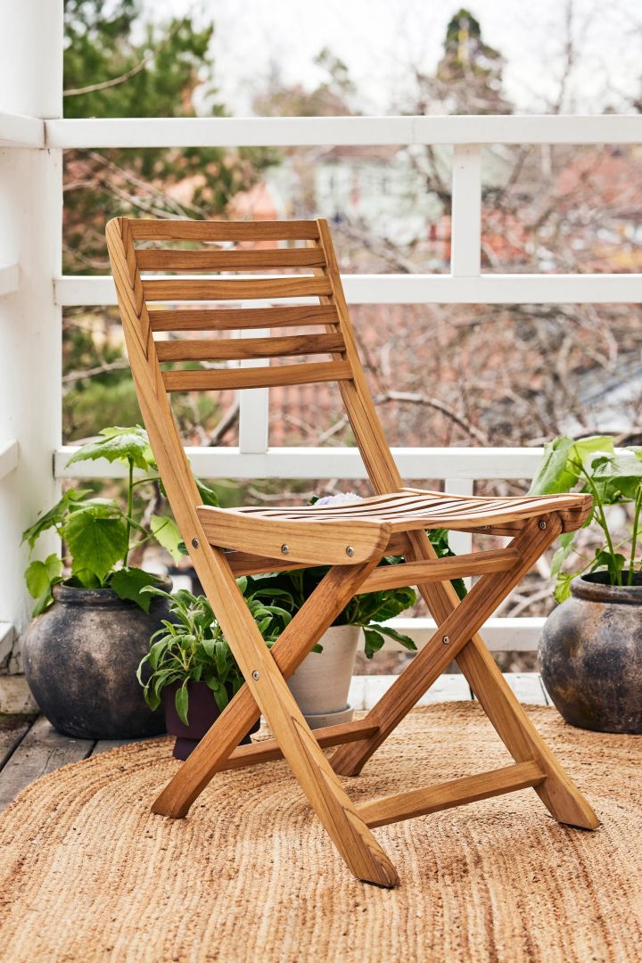 The folding teak Aneboda chair from 1898 seen here on a small balcony surrounded by plants. 