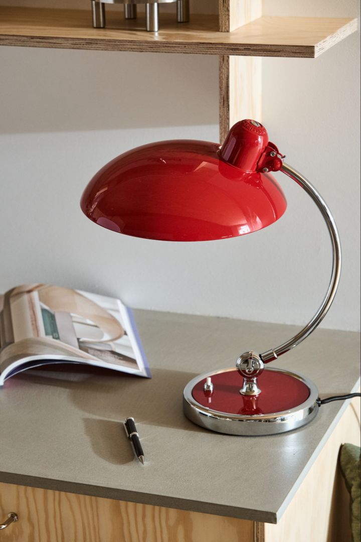 A close up of the Kaiser table lamp in ruby red with it's curved stainless steel stand. 