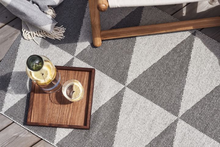 A wooden tray with a glass of lemon water sits on a plastic rug from Scandi Living, two summer essentials for you to enjoy. 