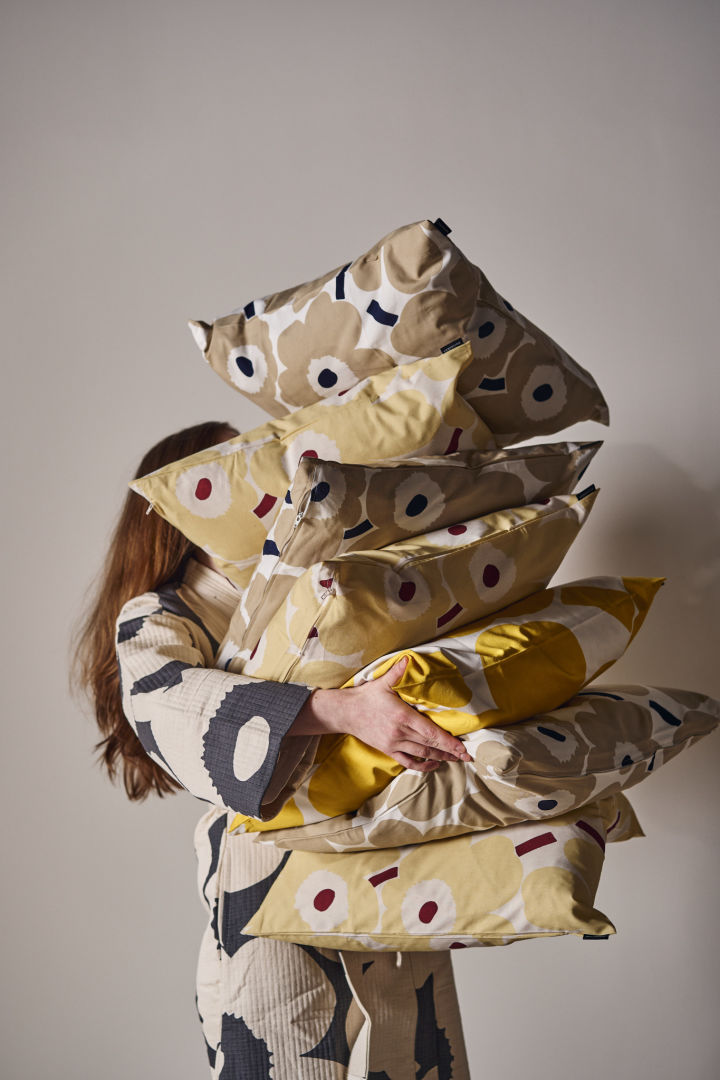 A woman carries a stack of unikko pillows in her arms.