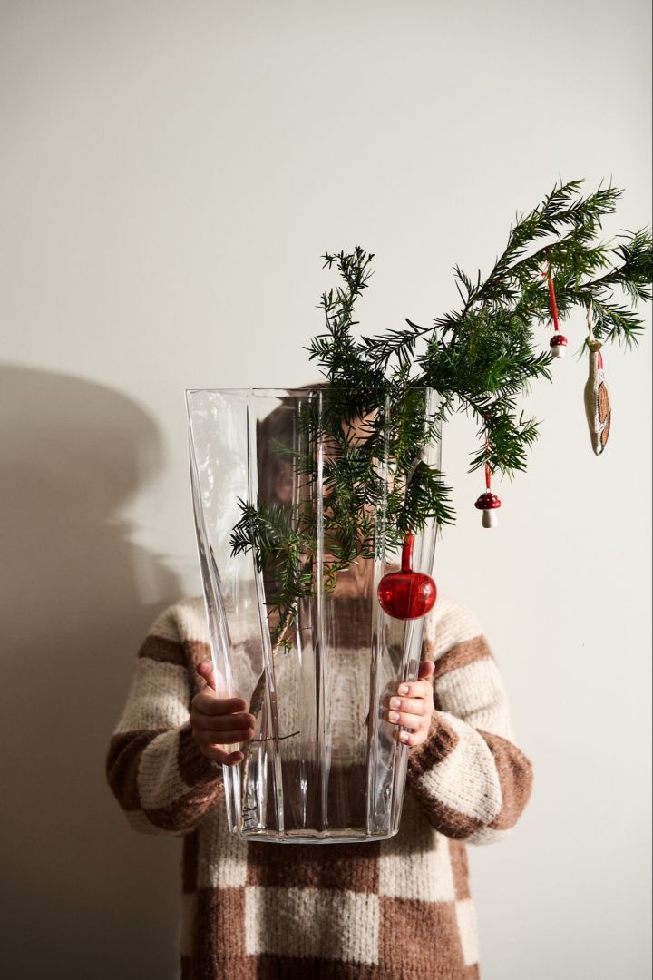 Someone holds out the Reed vase from Orrefors with a pine garland and some vintage Christmas decorations.  