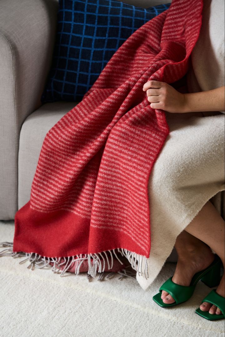A woman sits on a sofa with the red wool throw from NJRD, part of the vintage Christmas decor. 