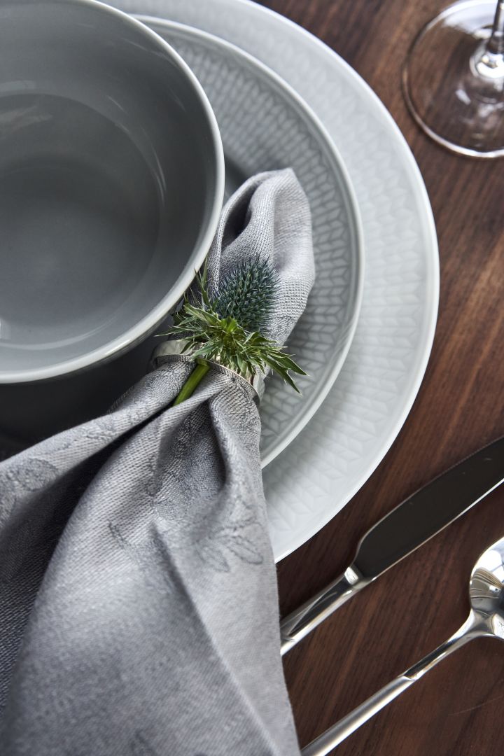 Table setting with Swedish Grace porcelain in white and grey and linen napkin in napkin ring with flowers as a decoration. 