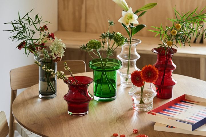 A collection of red, green, grey and clear vases stand on a table with a red and blue backgammon set. 