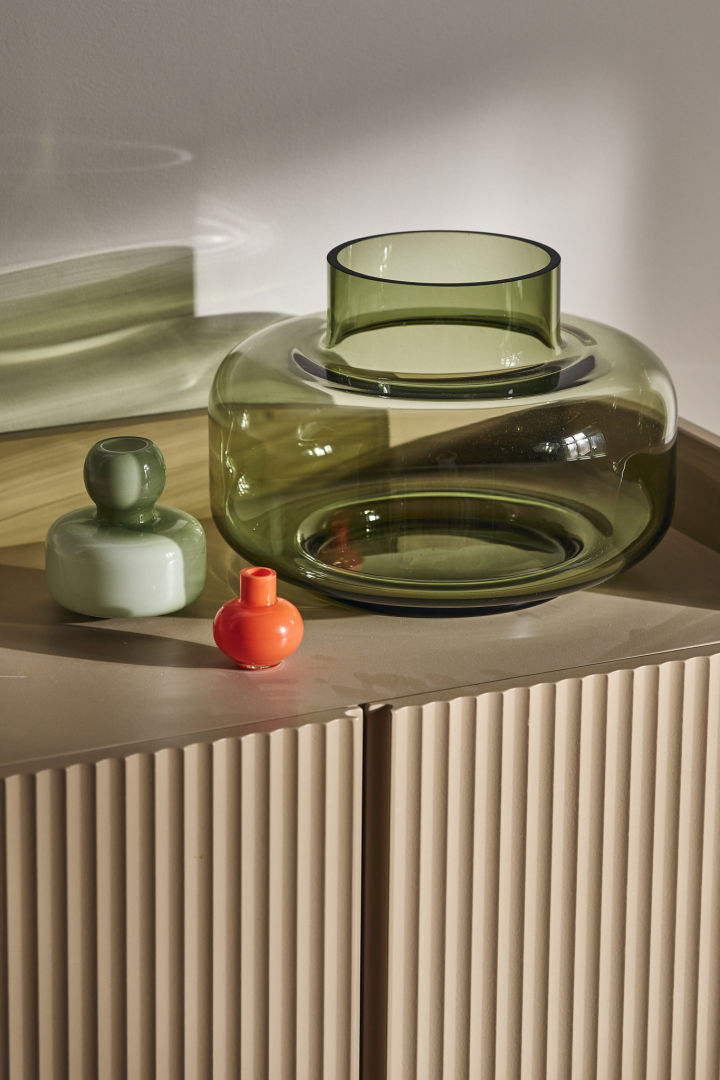 The Urna vase in green from Marimekko stands on a cupboard with the mini vase in orange.