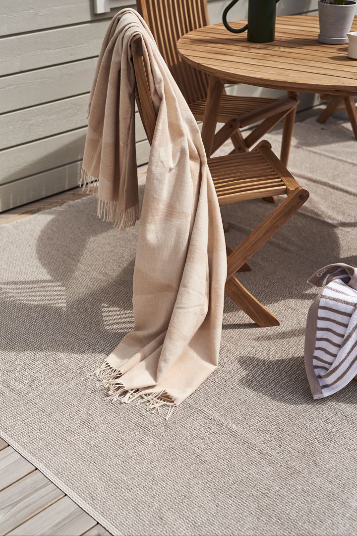 The Mellow plastic rug from Scandi Living, draped over a teak chair, the perfect idea for a balcony. 