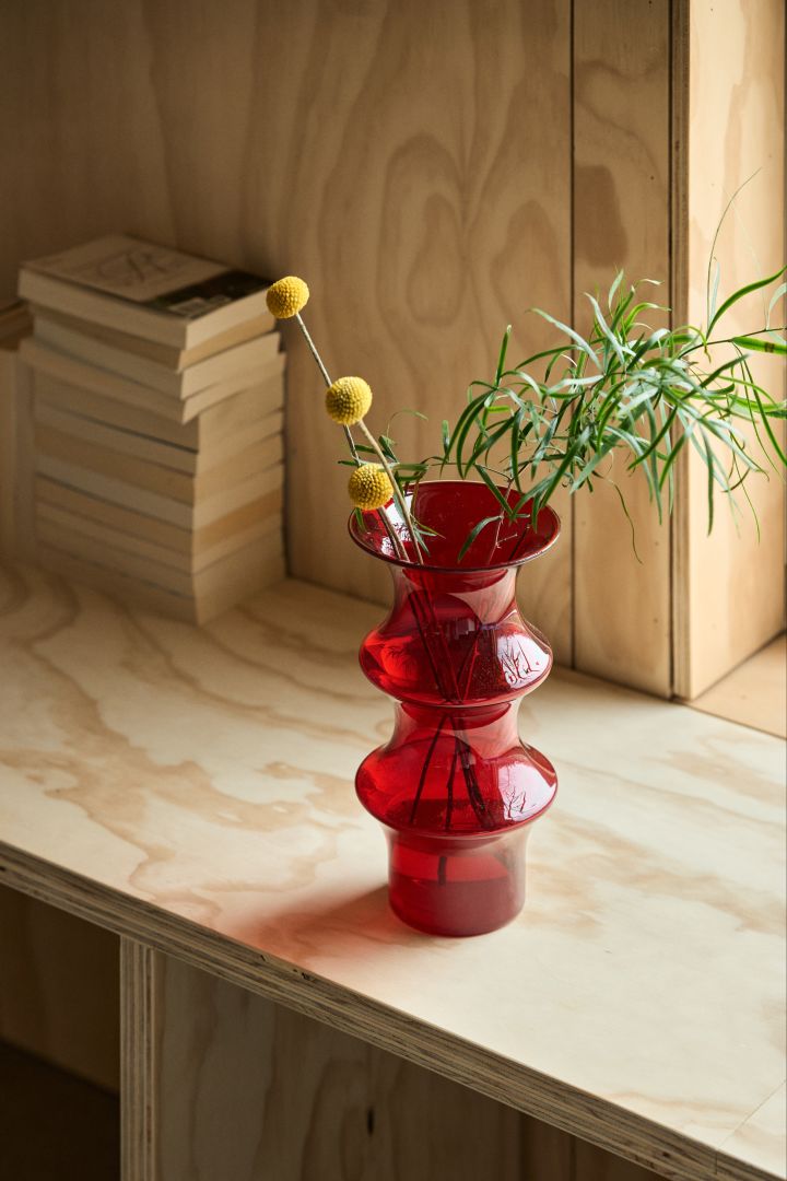 The autumn 2023 season's interior design trends include playful shapes in colour, like this red glass vase from Kosta Boda with yellow flowers.