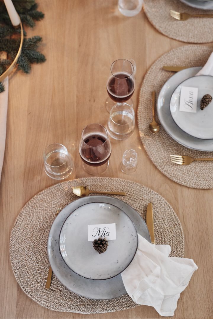 A white Christmas table decoration with a place setting consisting of rustic stoneware plates, gold cutlery and a white linen napkin.